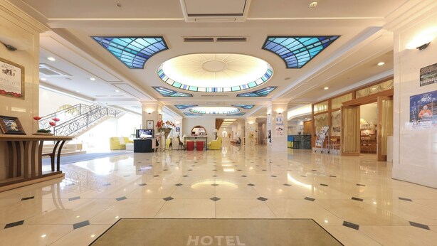 A hotel lobby with a polished floor, a central reception desk, and a staircase. - HOTEL LiVEMAX Numata GRANDE (Numata)