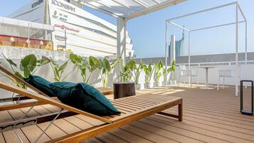 A wooden deck with a lounge chair, potted plants, and a view of a modern building.