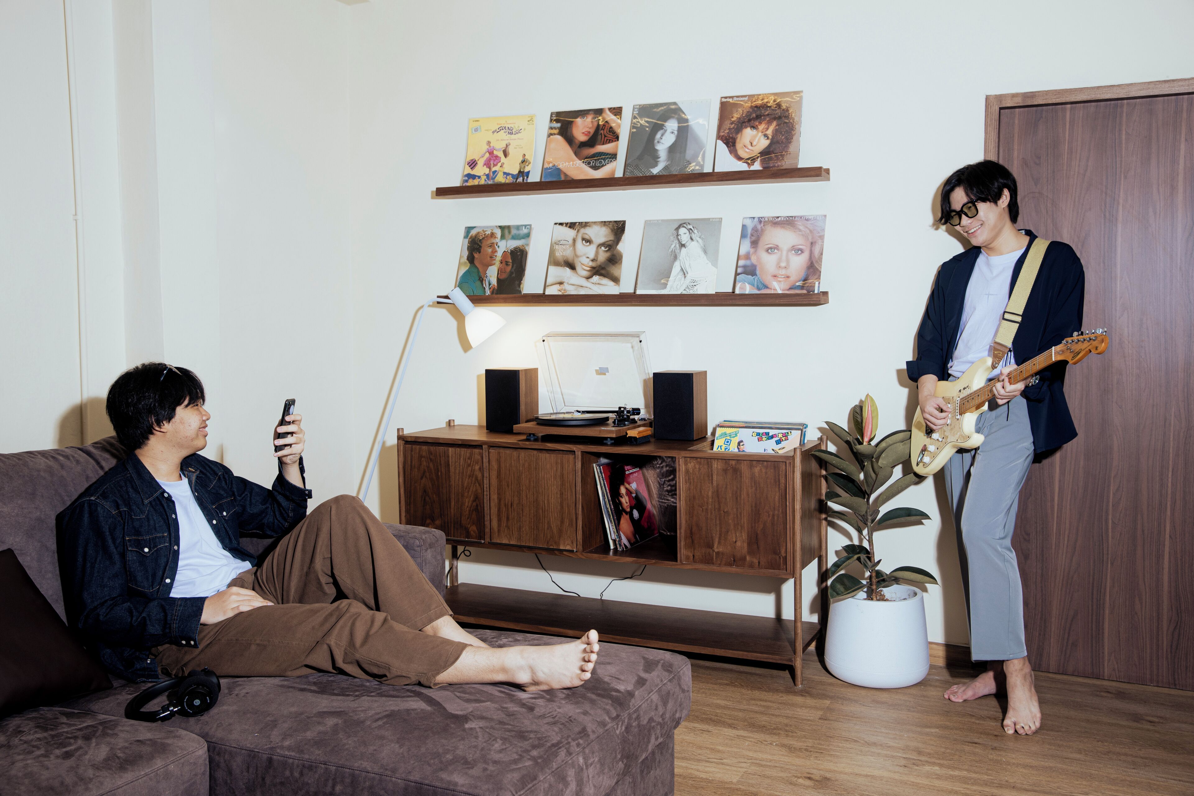 A living room with a couch, a wooden cabinet with pictures, a plant, and a person playing a guitar.