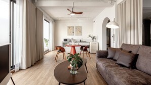 A modern living room with a brown sofa, a round coffee table with a plant, and a dining area with a red table and chairs. - The Lair Bangkok (Bangkok)