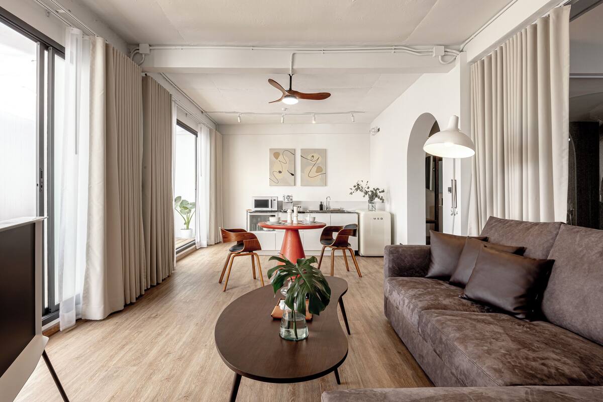 A modern living room with a brown sofa, a round coffee table with a plant, and a dining area with a red table and chairs.