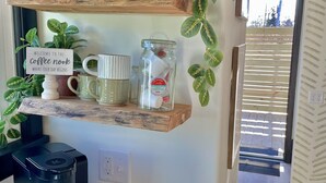A kitchen with wooden shelves holding mugs, a coffee maker, and a sign reading "Welcome to the coffee nook."