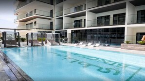 Un edificio moderno con zona de piscina, que incluye sillones de descanso y una sección con cerramiento de vidrio.