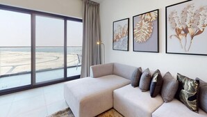 Una sala de estar moderna con un ventanal amplio, un sofá seccional color beige y tres cuadros con motivos florales en la pared.