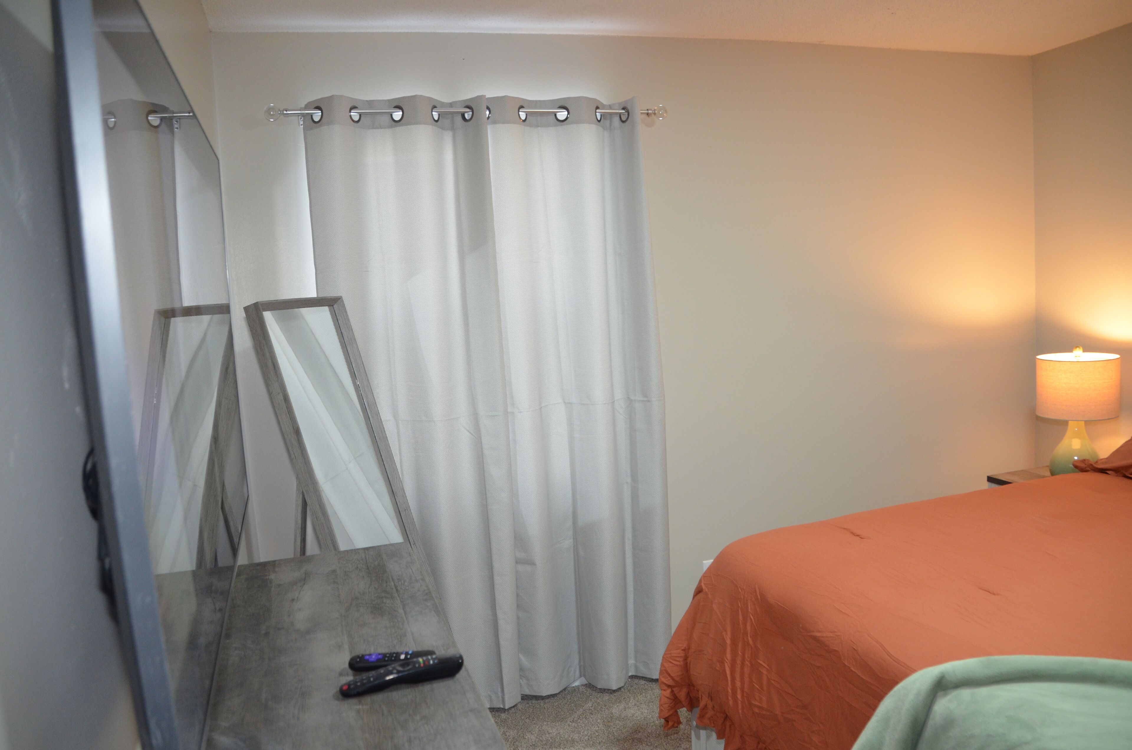Une chambre d’hôtel avec un lit, une lampe, un miroir et un rideau.