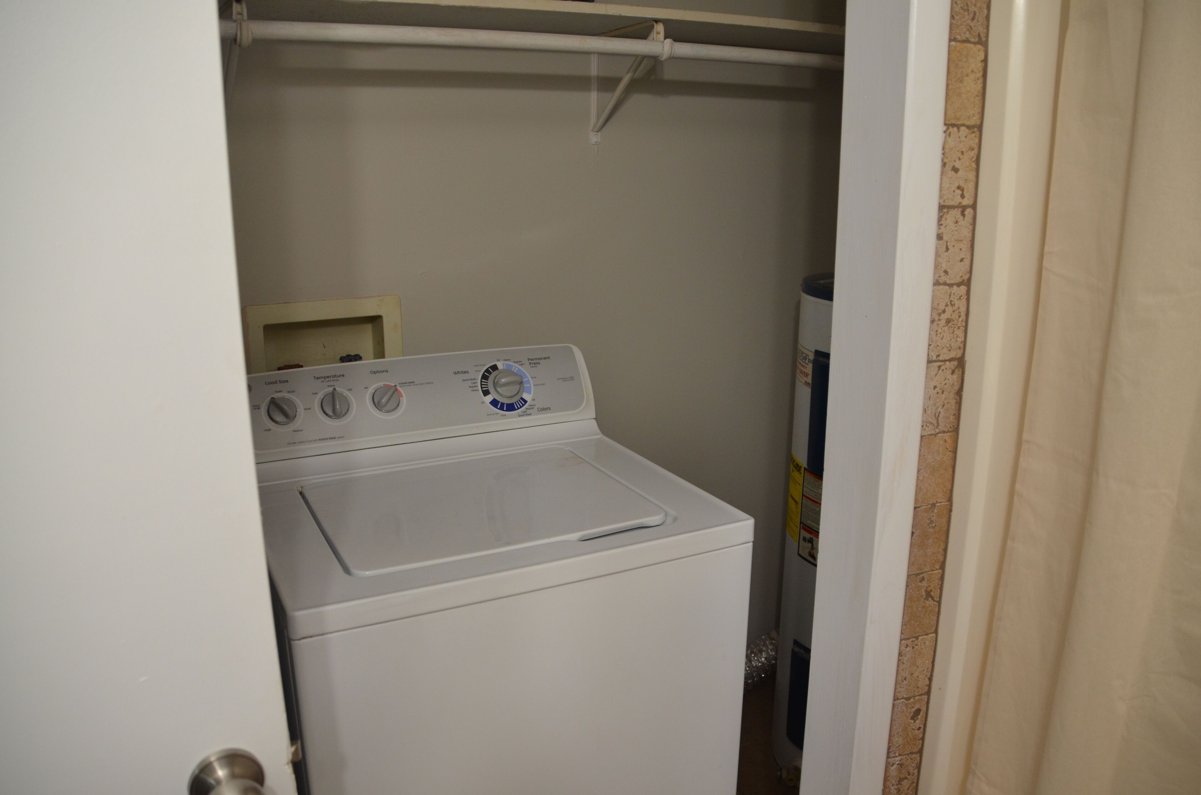A compact laundry room with a front-loading washer and dryer, a towel rack above the dryer, and a door leading to another room.