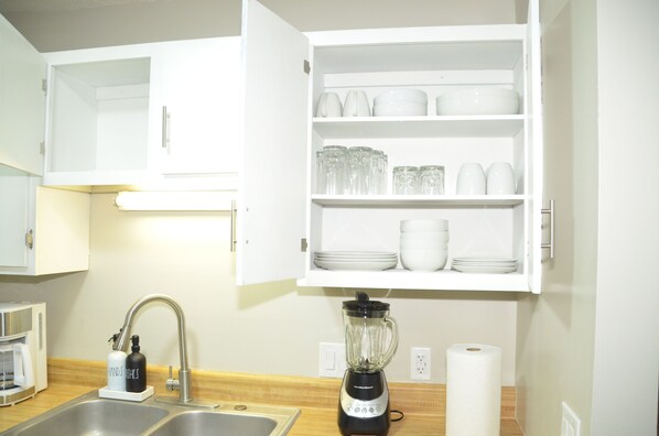 A kitchen with a white cabinet containing dishes and glasses, a coffee maker, and a blender. - Enchanting Oasis - Centrally located! Quiet, great TDY spot, family friendly. (Enterprise)