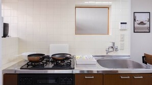 A kitchen with white tiled walls, a stainless steel sink, a gas stove, and wooden cabinets.