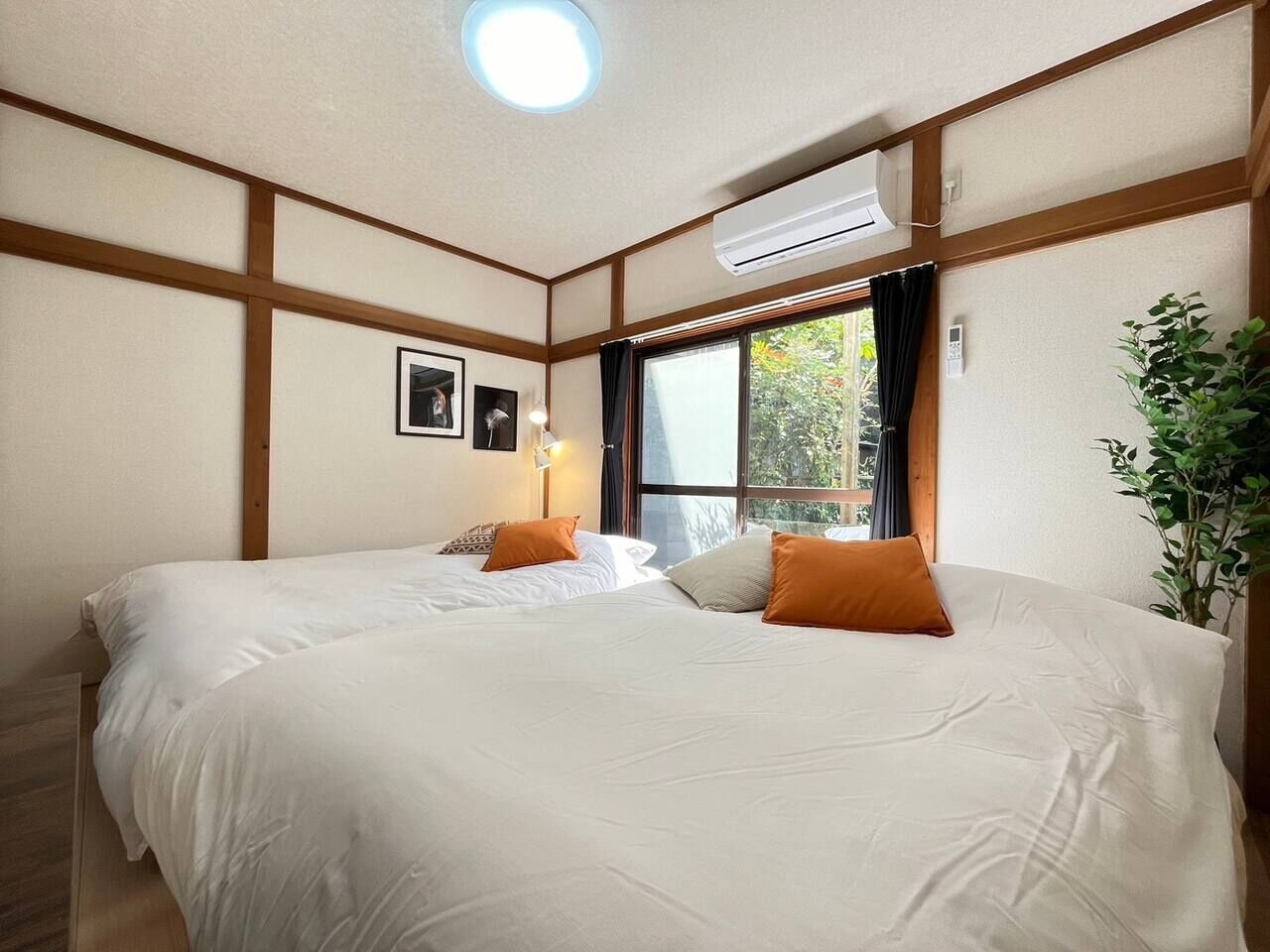 Habitació d'hotel amb un llit gran, un aparell d'aire condicionat, una finestra amb cortines i una planta.