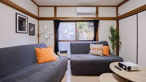 A compact living space with two grey sofas, one with an orange pillow and the other with a patterned pillow. A small wooden table with a projector and remote control is in the foreground.