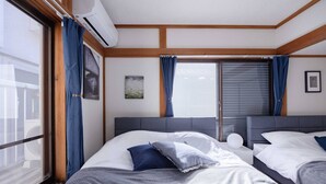 A hotel room with two beds, a large window with curtains, an air conditioning unit, and a view of the outside.
