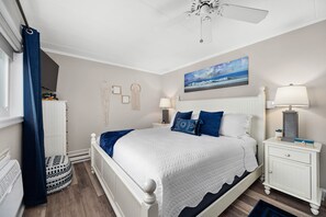 A bedroom with a white bed, blue bedding, a white nightstand, a lamp, and a ceiling fan. - Exquisite Ocean View Condo with Pool (Ocean City)