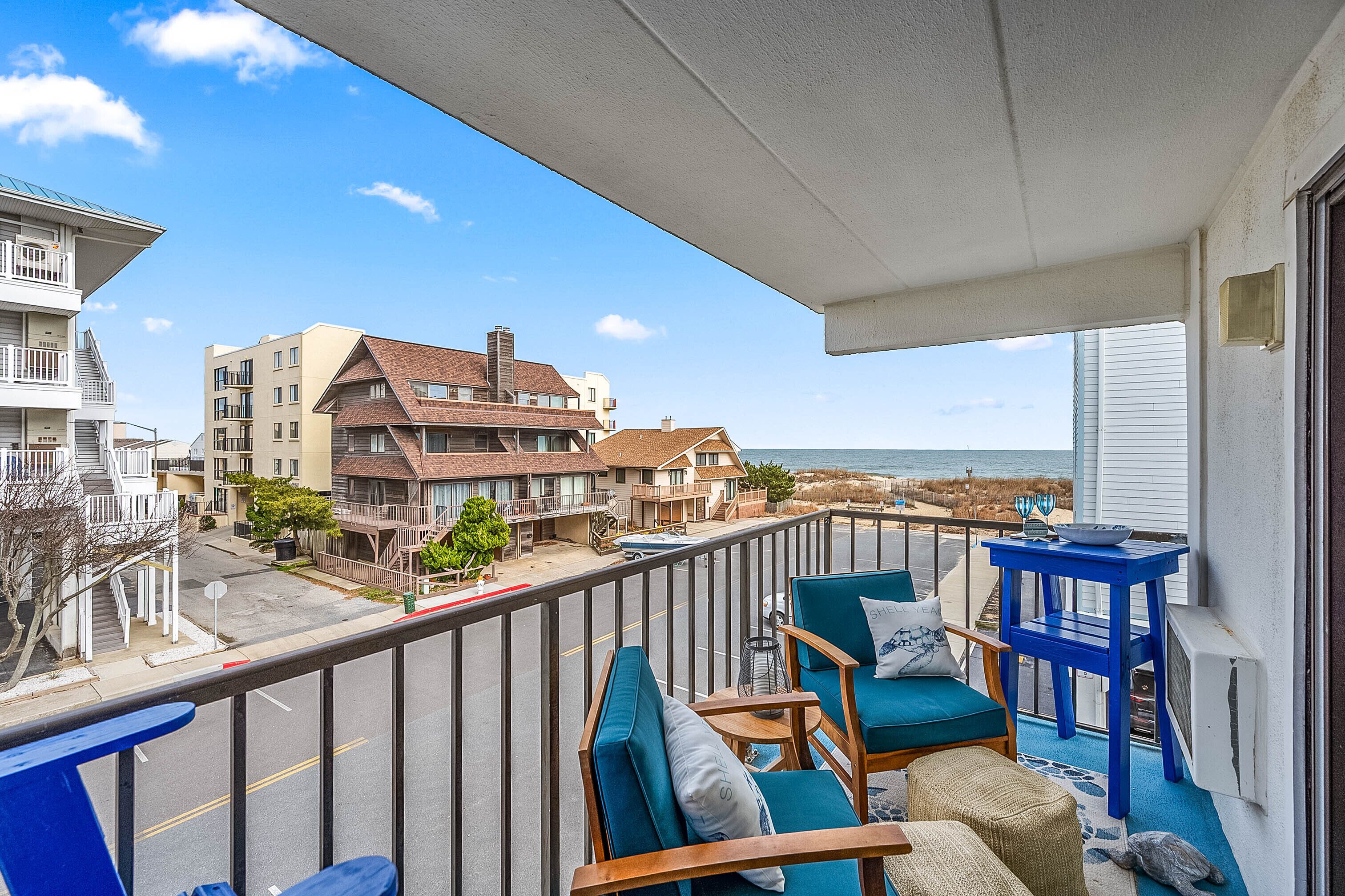 A balcony with a view of the ocean, wooden furniture, and a blue table.