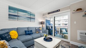Un salon avec un canapé d’angle gris, une table basse blanche et une vue sur un balcon aménagé avec du mobilier d’extérieur.