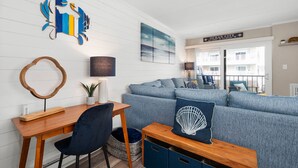 Un salon moderne avec un canapé bleu, un bureau en bois et une œuvre d’art accrochée au mur.