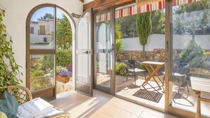 A sunlit patio with a wooden ceiling, a glass door leading to a garden, and a table with chairs. - El Rinconcito by Interhome (Moraira)