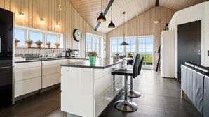 Een moderne keuken met een centraal eiland, houten plafond en grote ramen met uitzicht.