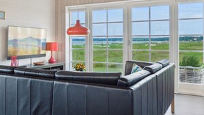 Een moderne woonkamer met een zwarte leren bank, een rode hanglamp en een groot raam met uitzicht op een groen landschap.