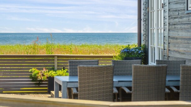 Een houten gebouw met uitzicht op de oceaan. Er staan buiten tafels en stoelen.