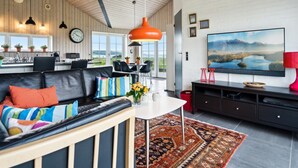 Een moderne woonkamer met een zwarte leren bank, een ronde salontafel en een grote flatscreen televisie aan een witte muur.
