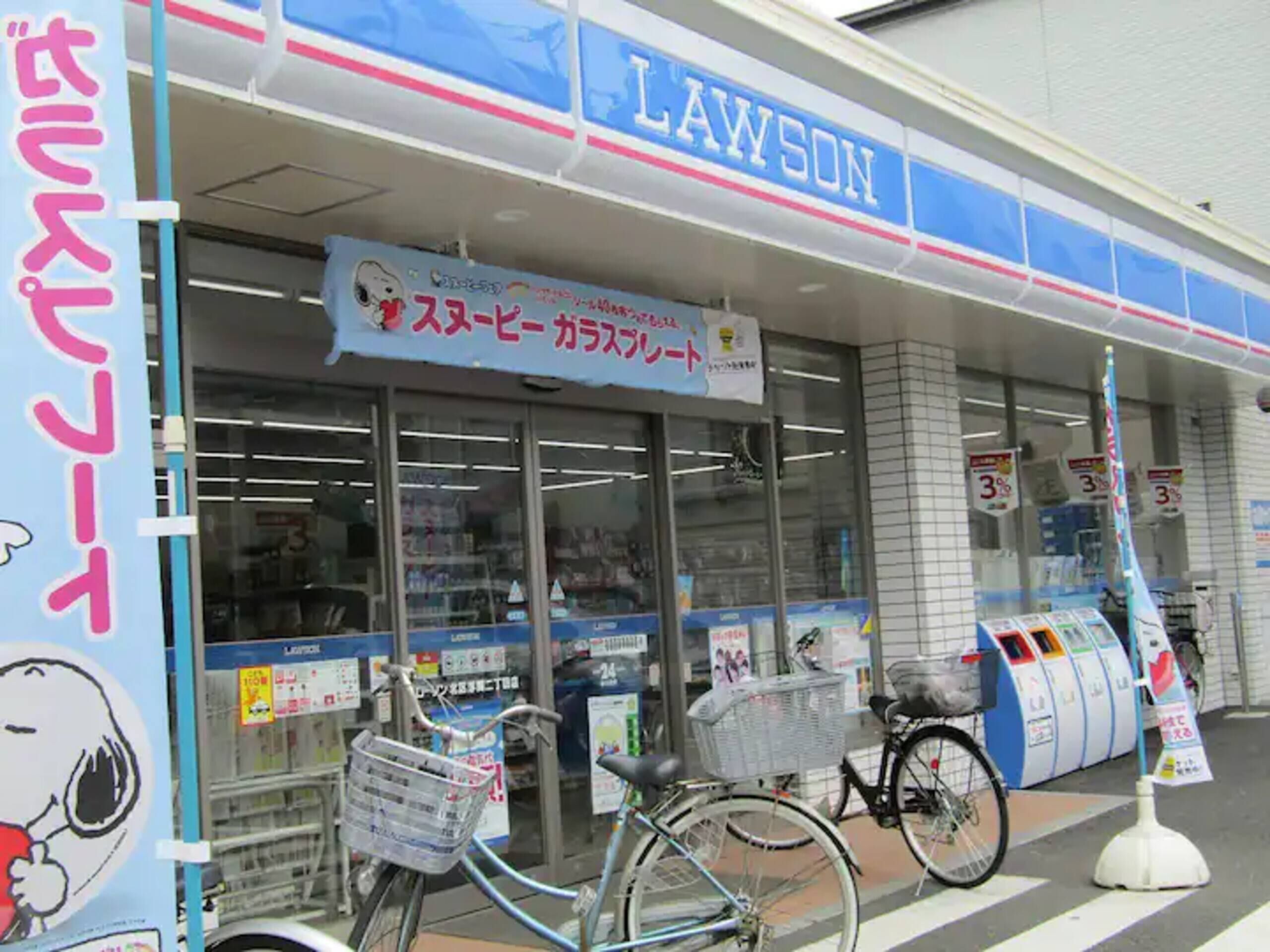 Un negozio Lawson con un grande cartello, una bicicletta parcheggiata fuori e un carrello della spesa.