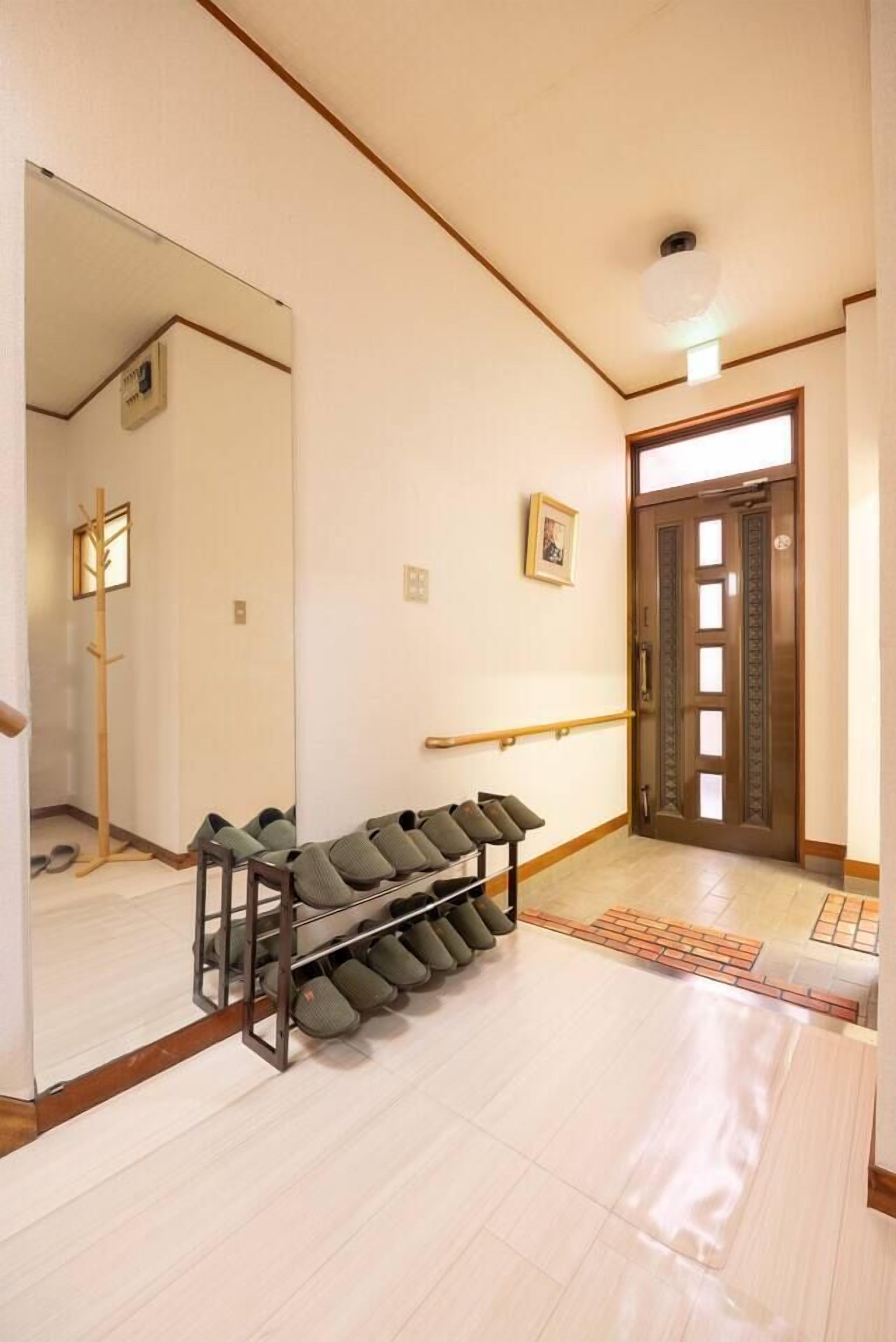 A hallway with a shoe rack, a wooden door, and a mirror reflecting the room.