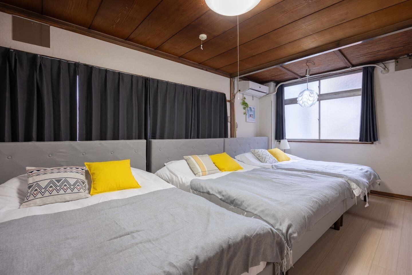 Ein Zimmer mit zwei Betten, dunklen Vorhängen, einer Holzbalkendecke und einem Fenster mit Blick.