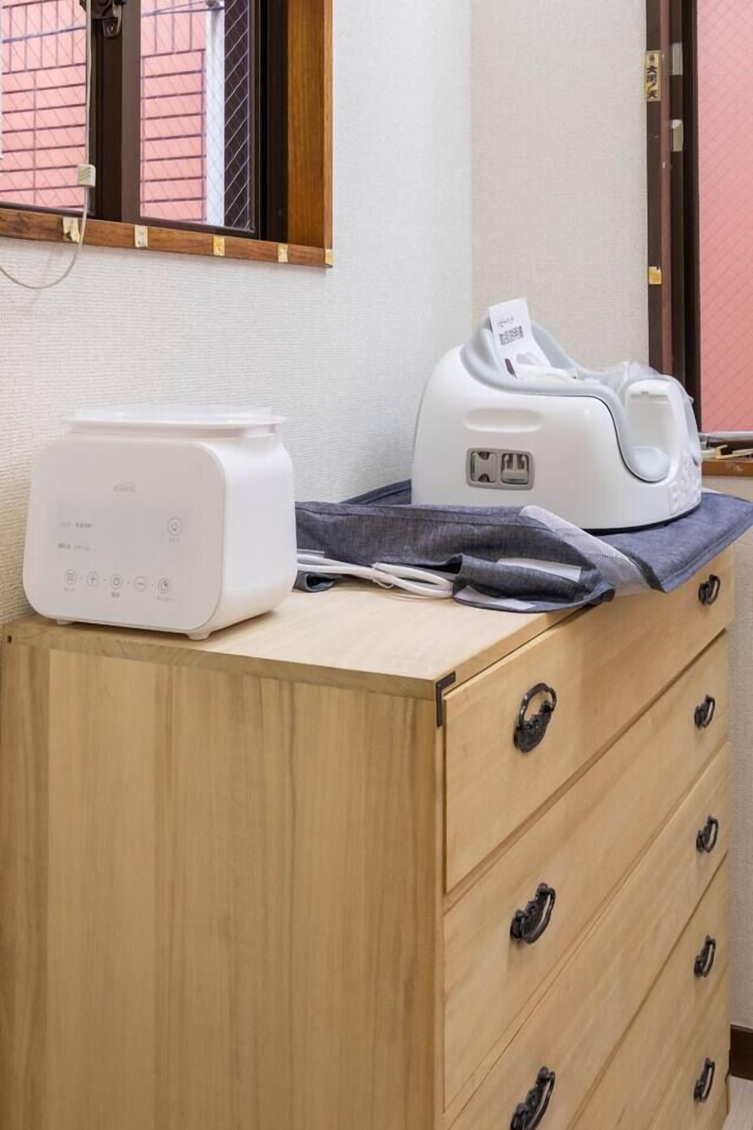 Une commode en bois sur laquelle est posé un appareil électroménager blanc, un tissu gris et une fenêtre à carreaux.
