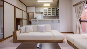 A modern living room with a white sofa, wooden accents, and a kitchen area in the background.