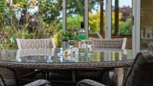 A round glass table with wicker chairs, a bottle of wine, and a small potted plant.