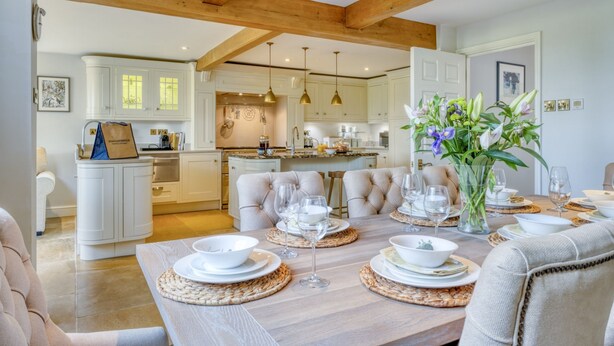 A dining area with a wooden table set for a meal, surrounded by cushioned chairs.