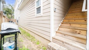 Ein Haus mit einer Holztreppe, die zu einer Veranda führt, einem Grill und einem Propangasbehälter.