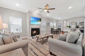 A modern living room with a fireplace, grey sofas, a dining area, and a kitchen. - Romana Hideaway-Main House, Downtown, New Listing! (Pensacola)