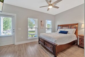 A bedroom with a wooden bed, a ceiling fan, and large windows with blinds. - Romana Hideaway-Main House, Downtown, New Listing! (Pensacola)