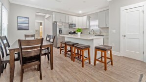 A modern kitchen with white cabinets, a central island, bar stools, and a dining table with chairs. - Romana Hideaway-Main House, Downtown, New Listing! (Pensacola)