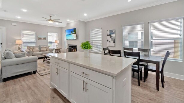 A modern kitchen with a central island, dining area with chairs, and a living room with a sofa and TV. - Romana Hideaway-Main House, Downtown, New Listing! (Pensacola)