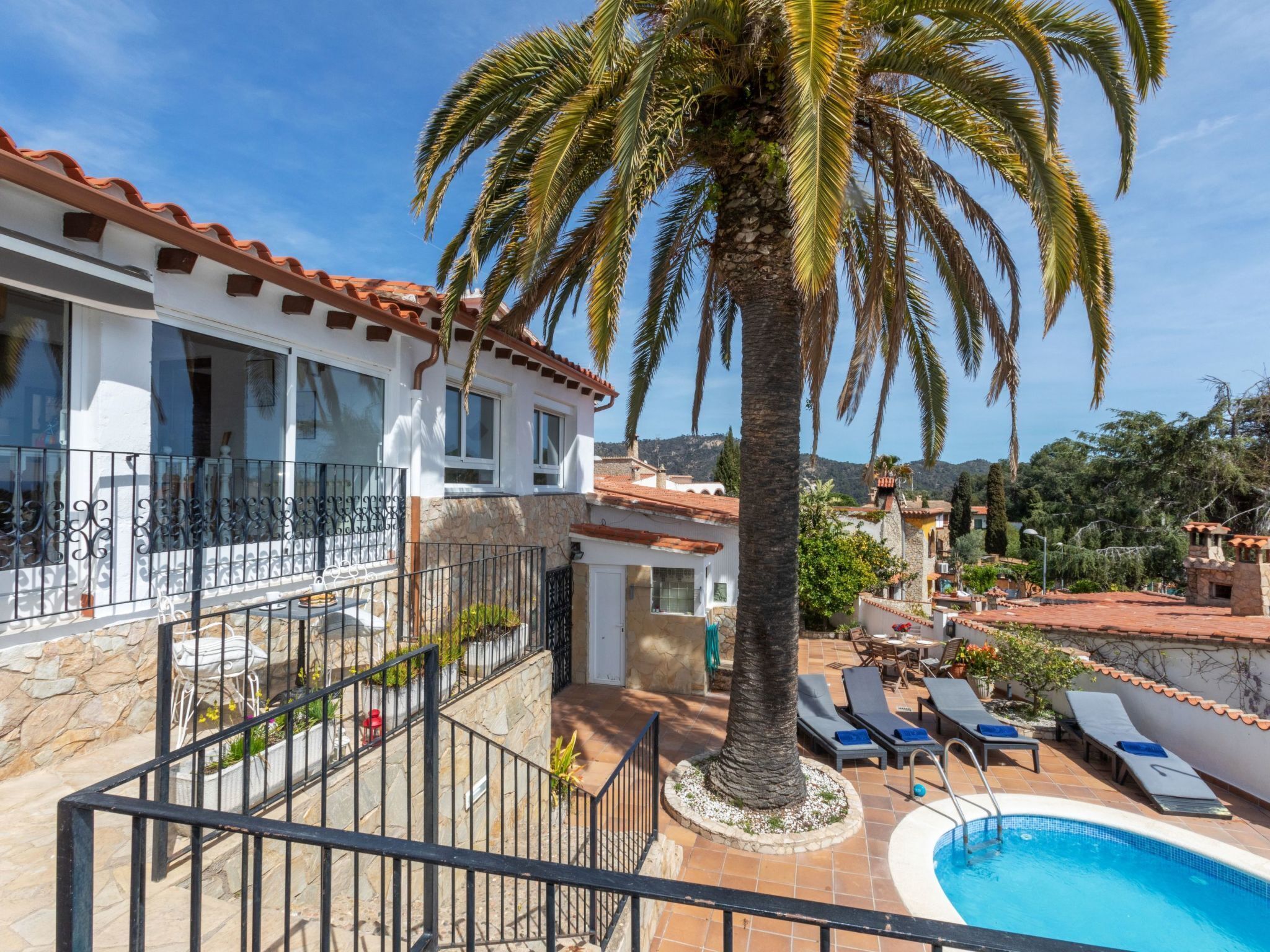 A villa with a swimming pool, palm trees, and a view of the hills.