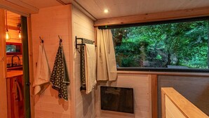 L’intérieur d’un chalet rustique, avec des murs en bois, une fenêtre avec des rideaux, un banc en bois et un petit four vitré.
