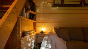 Une chambre mansardée chaleureuse avec un plafond en pente en bois, une petite table de chevet avec une lampe et un banc rembourré.