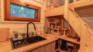 Une cuisine en bois dotée d’un évier encastré, d’une fenêtre située au-dessus de l’évier et d’étagères en bois où sont rangés les ustensiles de cuisine.