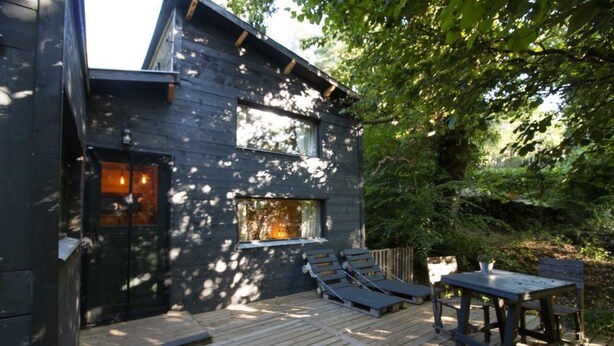 Une terrasse en bois, agrémentée de chaises longues et d’une table, entourée d’une végétation luxuriante.