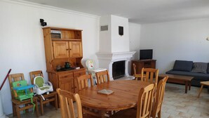 Ein Essbereich mit Holztisch und -stühlen, eine Küche mit Holzschränken, ein Kamin und ein Fernseher im Wohnzimmer.