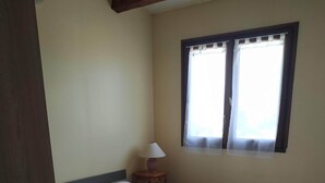 Ein Einzelbett mit weißer Bettwäsche in einem Zimmer mit Holzboden und einem Fenster mit durchsichtigen Vorhängen.