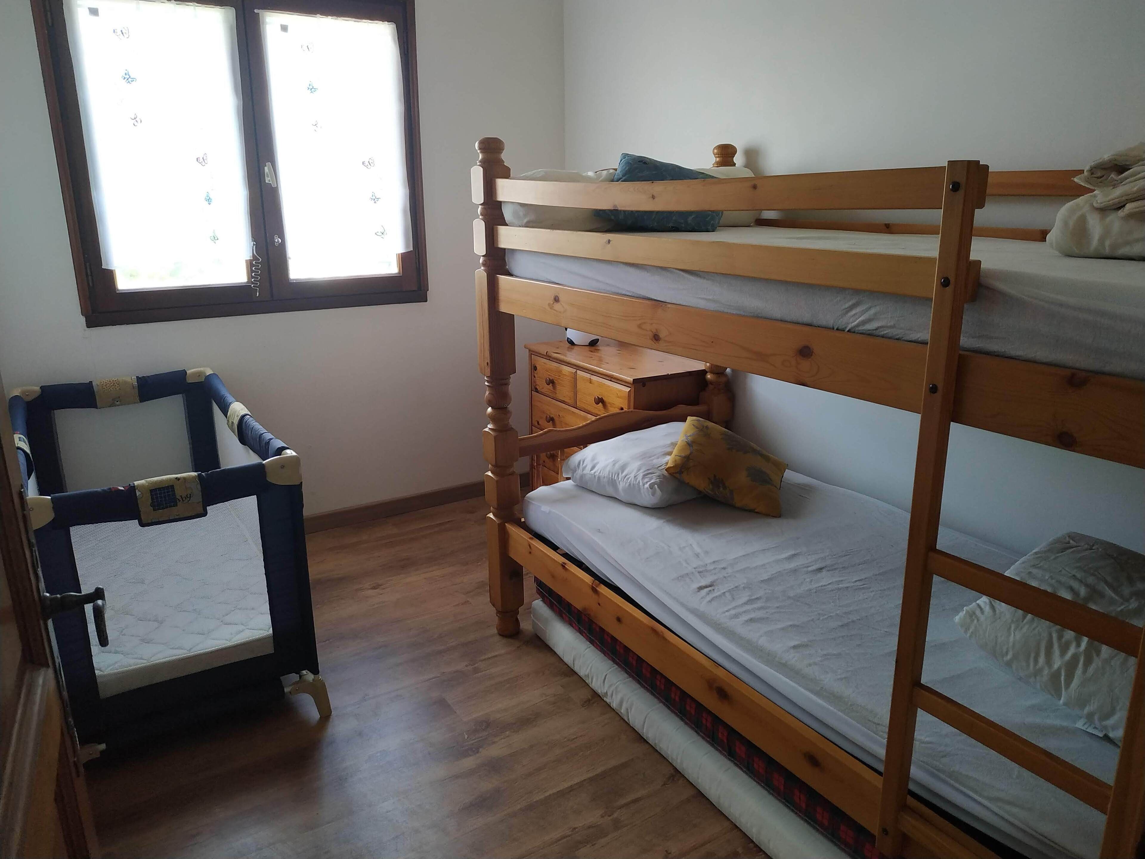 A room with a bunk bed, a small wooden dresser, and a baby playpen.