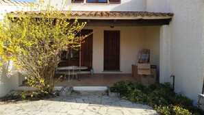 Ein Haus mit Ziegeldach, einer Haustür und einer kleinen Veranda mit Tisch und Stühlen.
