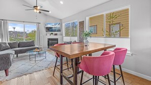 Ein modernes Wohnzimmer mit Essbereich, Deckenventilator, großen Fenstern und Kamin.