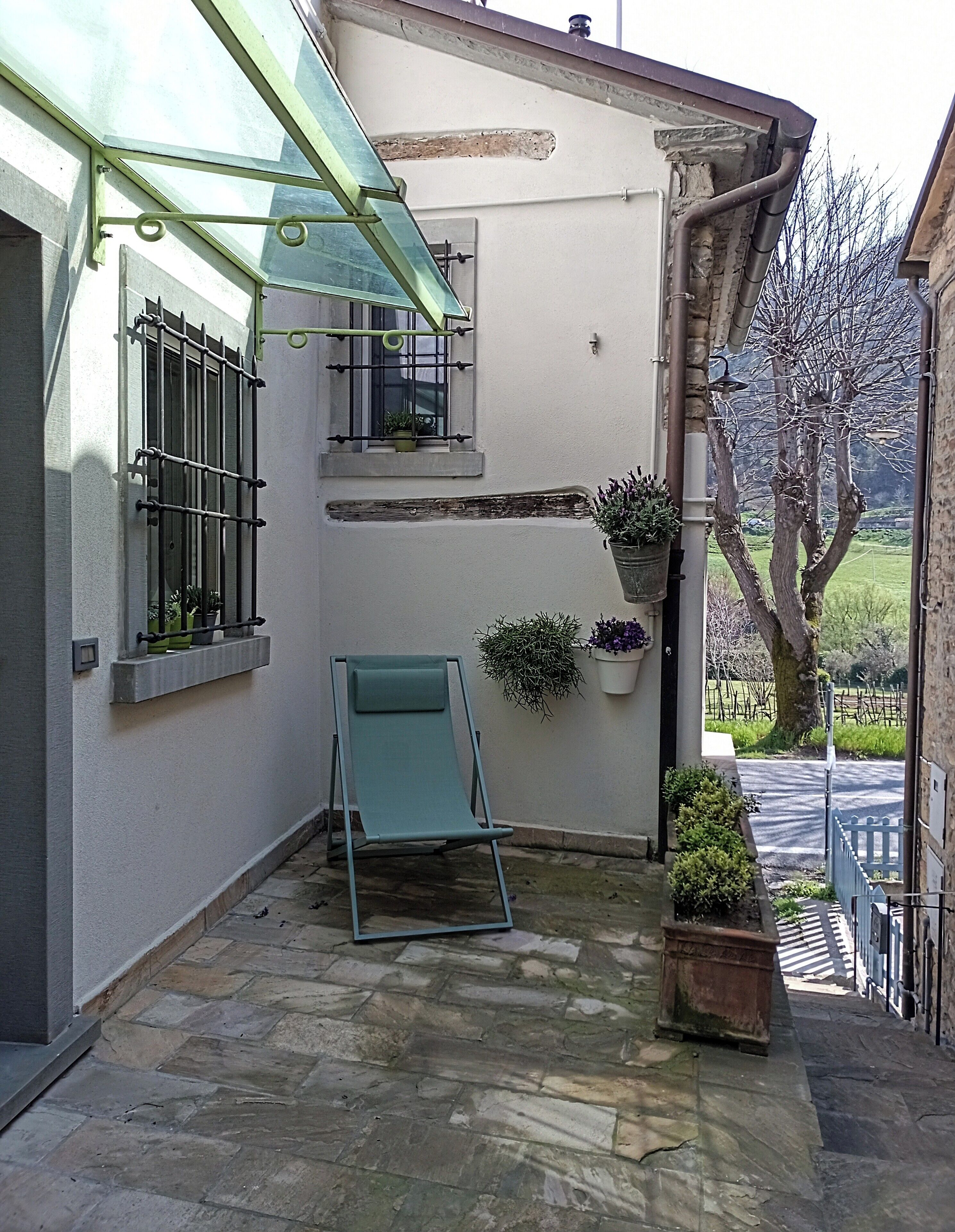 A stone-floored patio with a green lawn chair, potted plants, and a glass-enclosed window.