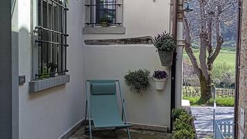 A stone-floored patio with a green lawn chair, potted plants, and a glass-enclosed window.