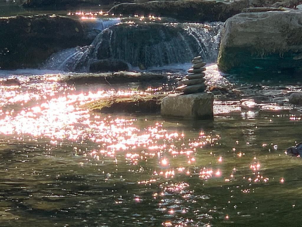 Eine friedliche Landschaft mit einem Wasserfall, einer Steinhaufen und einer spiegelnden Wasseroberfläche.