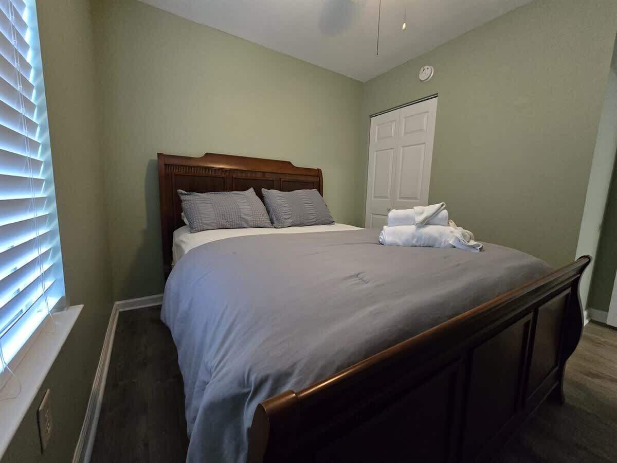 A bedroom with a wooden bed frame, a grey bedspread, and a white door in the background.